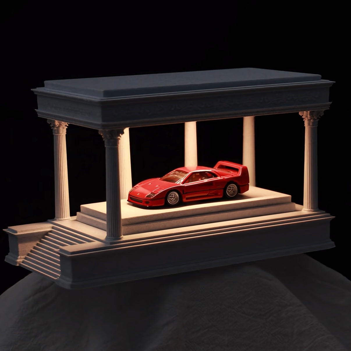 Red car model on a decorative platform with columns against a black background