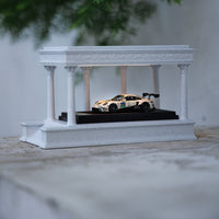 Model car on a white display stand with columns against a neutral background