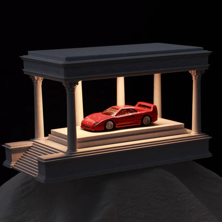 Red car model on a decorative platform with columns against a black background